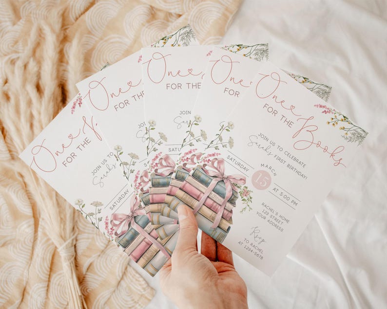K&ouml;nnte beinhalten: Rosa und wei&szlig;e Einladung zu einem ersten Geburtstag mit dem Text "One for the Books" und einem Stapel B&uuml;cher mit einem rosa Band. Die Einladung enth&auml;lt Datum, Uhrzeit und Ort der Party.