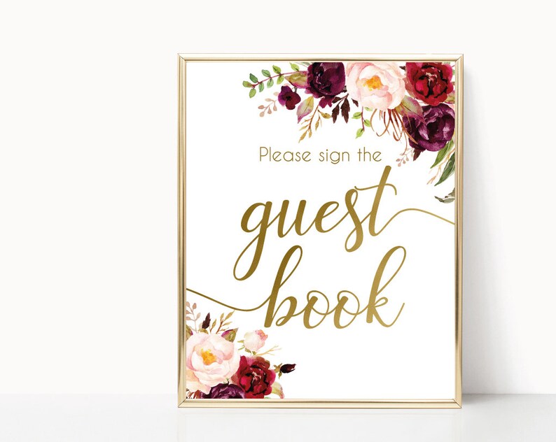 K&ouml;nnte beinhalten: Goldenes Schild mit burgunderrotem und rosafarbenem Blumendesign. Das Schild lautet "Bitte unterschreiben Sie das G&auml;stebuch".