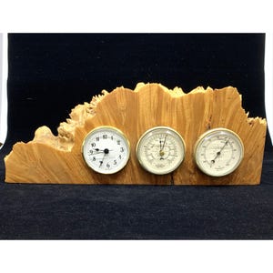 May include: A wooden desk clock with a barometer and thermometer. The clock has a white face with black numbers and hands. The barometer and thermometer have white faces with black markings. The wooden base has a natural wood grain.