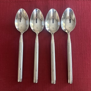 May include: Four silver spoons with a floral design on the bowl. The spoons have a simple, elegant design with a long, slender handle. The spoons are arranged on a red surface.