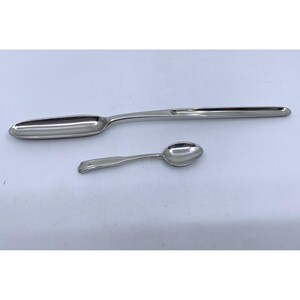 May include: Two silver spoons. One is a long, slender serving spoon with an oval bowl. The other is a smaller spoon with a rounded bowl and a decorative handle. Both spoons are made of shiny metal.