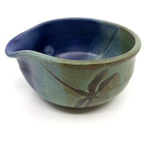 May include: A ceramic mixing bowl featuring a deep blue interior and a mottled green and brown exterior. The bowl has a distinct pouring spout on one side and a dark, silhouette-style dragonfly graphic imprinted on the outer surface of the vessel.