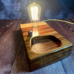 May include: A wooden lamp base with a light bulb and a switch. The base has a small, rectangular recess in the top.