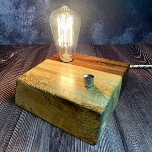 May include: A wooden table lamp with a vintage-style light bulb and a toggle switch. The lamp is made of natural wood and has a rustic look.