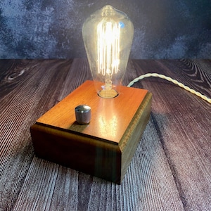 May include: A wooden lamp base with a vintage-style light bulb and a silver knob switch. The lamp is on a dark wood surface.