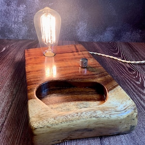 May include: A wooden lamp base with a light bulb and a switch. The base is made of dark wood with a light wood inlay. The lamp is on a wooden surface.