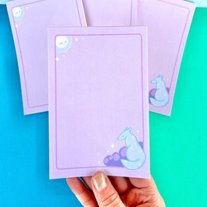 May include: Four lavender colored notepads with a white cloud and sun design in the top left corner. The bottom right corner of each notepad features a blue and yellow spotted animal with a white cloud and stars.