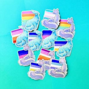 May include: A collection of stickers featuring stylized blue and purple cat-like creatures with star accents. Each sticker includes a rainbow or pride flag design. The stickers are arranged on a bright teal background.