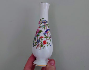 Puede incluir: Un jarrón de cerámica blanco con un diseño floral y de pájaros. El jarrón tiene un borde festoneado y un borde dorado alrededor de la base.