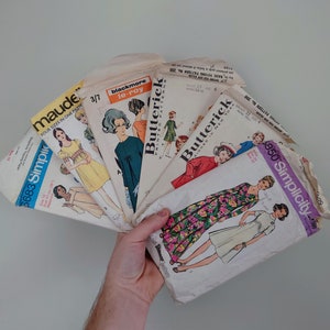Puede incluir: Una colección de patrones de costura vintage para ropa, incluyendo Simplicity, Butterick y Maude. Los patrones son de varios colores, incluyendo blanco, rosa, azul y verde. Los patrones presentan ilustraciones de mujeres usando los diseños de ropa.