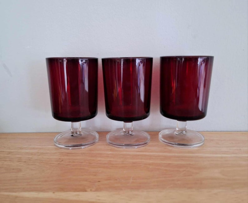 May include: Three clear glass wine goblets with a deep red colored base. The goblets have a short stem and a round base.