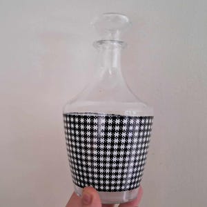 May include: A clear glass decanter with a black and white checkered pattern around the middle.