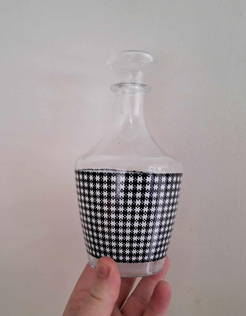 May include: A clear glass decanter with a black and white checkered pattern around the middle.