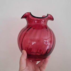 Può includere: Un vaso di vetro rosso con un bordo arricciato e un design a coste.