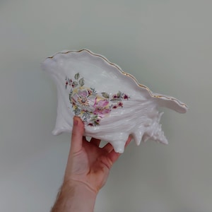 Könnte beinhalten: Weiße Keramikschale mit goldener Verzierung und Blumenmuster. Die Schale ist mit rosa, gelben und grünen Blumen bemalt.