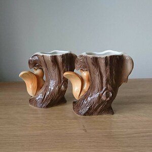 May include: Two ceramic planters shaped like tree stumps with squirrels on them. The planters are brown and have a textured surface.