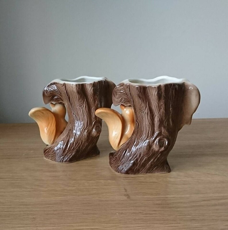May include: Two ceramic planters shaped like tree stumps with squirrels on them. The planters are brown and have a textured surface.
