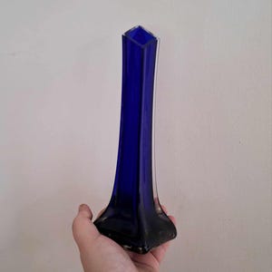 May include: A tall, cobalt blue glass vase with a square base and a narrow opening.