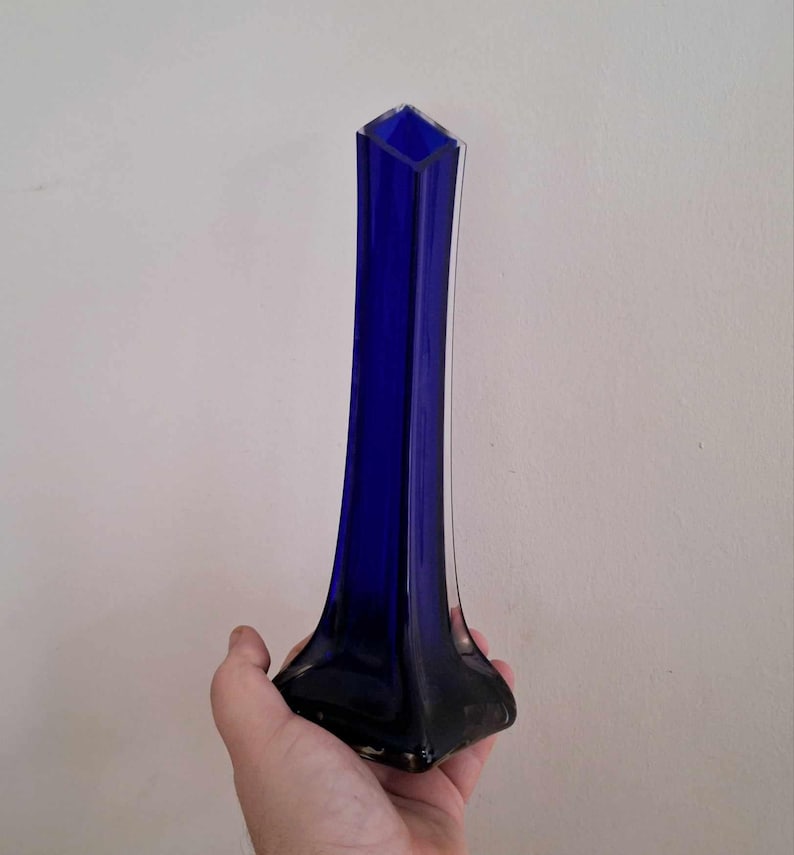 May include: A tall, cobalt blue glass vase with a square base and a narrow opening.