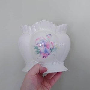 May include: White ceramic vase with a scalloped rim and a floral design featuring pink, purple, and green flowers.