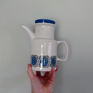 May include: White ceramic teapot with a blue lid and a black and blue geometric pattern around the body.
