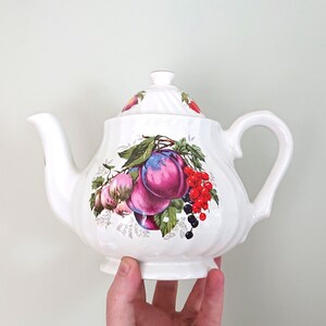 Théière vintage en céramique à motifs floraux violets et rouges, avec raisins. Idéale pour un thé de l'après-midi champêtre.
