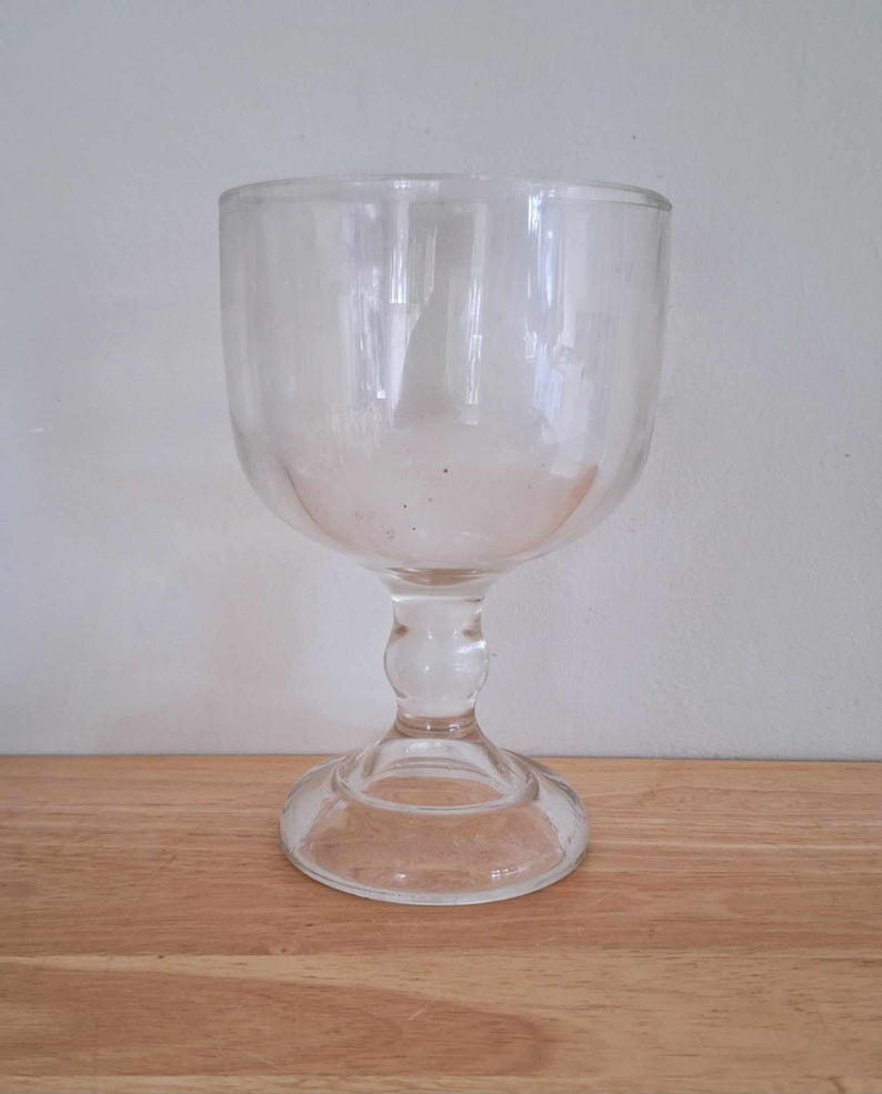 May include: A clear glass goblet with a wide bowl and a tall, slender stem. The goblet has a round base.