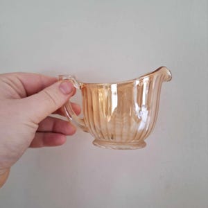 May include: A small, iridescent orange glass creamer with a fluted design and a handle.