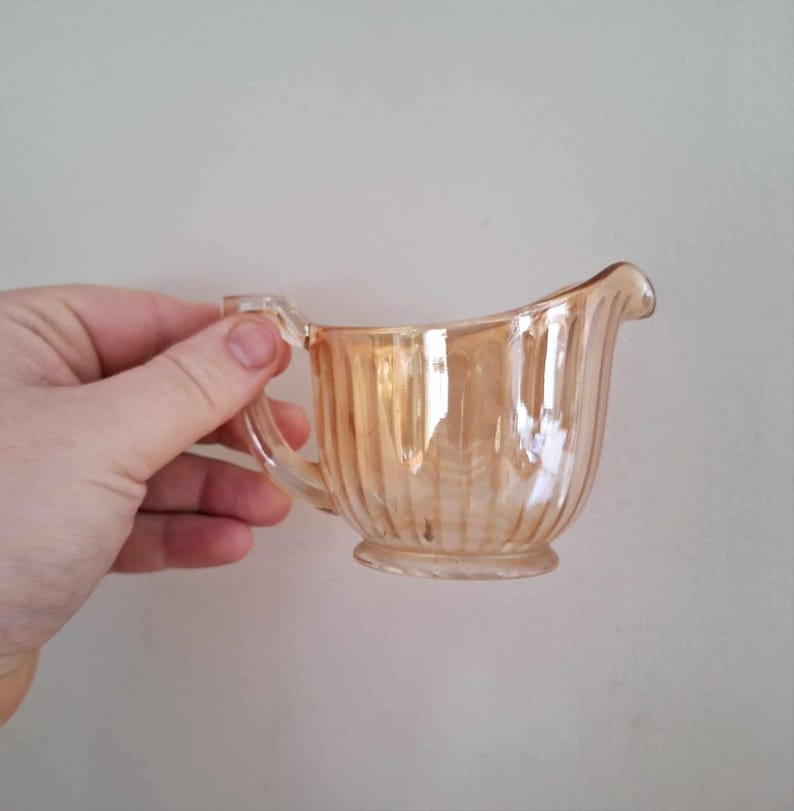 May include: A small, iridescent orange glass creamer with a fluted design and a handle.