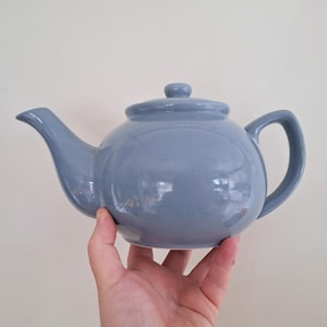 Puede incluir: Una tetera de cerámica azul claro con cuerpo redondeado y diseño sencillo.