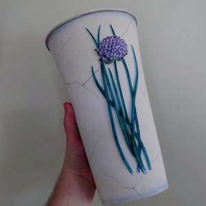 May include: White ceramic vase with a blue and purple flower design. The vase has a crackled glaze and a tall, cylindrical shape.