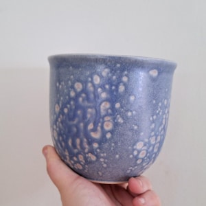 May include: A blue ceramic mug with a speckled glaze pattern. The mug has a rounded shape and a wide rim.