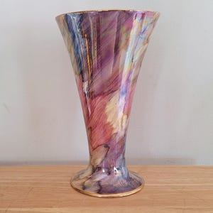 Könnte beinhalten: Eine hohe, irisierende Keramikvase mit einer ausgestellten, trompetenförmigen Öffnung und einem breiten, runden Boden. Die Vase ist mit einem wirbelnden Muster in Rosa, Lila und Gold verziert.