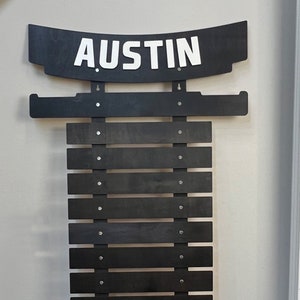 May include: A black wooden karate belt rack with the name "AUSTIN" in white letters on the top. The rack has 10 slots for belts.
