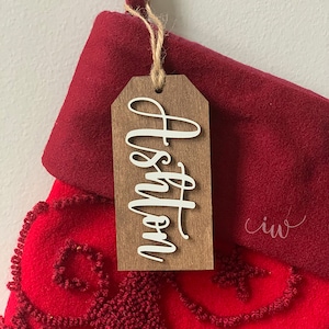 May include: A red stocking with a wooden tag that says "Merry" in white cursive lettering.
