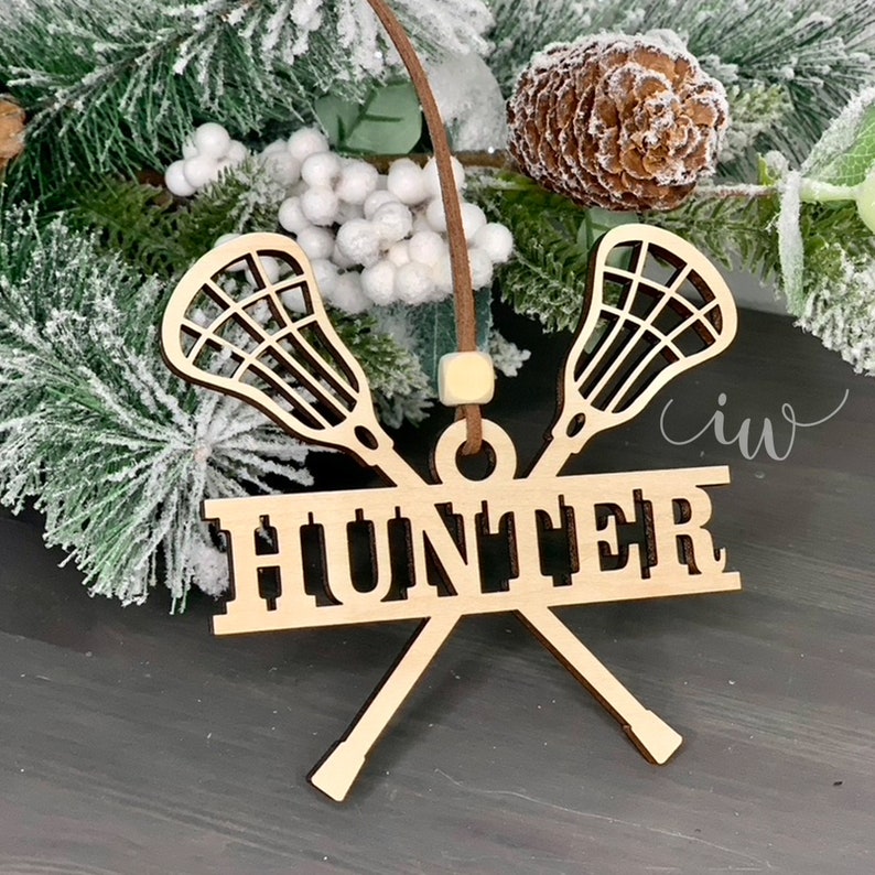 May include: Wooden lacrosse stick ornament with the name "Hunter" on it. The ornament is brown and has a white string for hanging.