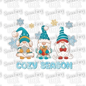 May include: Three gnomes with white beards and red hats are standing in front of a white background. The gnomes are wearing blue and white striped hats, blue and white patterned hats, and a blue hat with white stars. The gnomes are holding a red gift box, a snowflake, and a red ornament. The text "Cozy Season" is written in blue letters below the gnomes.