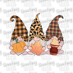 May include: Three gnomes standing side by side. The gnome on the left is holding a small orange pumpkin. The gnome in the middle is holding a brown and orange leaf. The gnome on the right is holding a brown cup with a swirl of whipped cream on top.