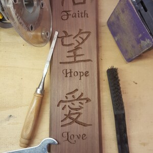May include: A wooden sign with the words "Faith", "Hope", and "Love" carved into it. The words are in both English and Chinese characters. The sign also includes the Bible verse "1 Cor. 13:13".