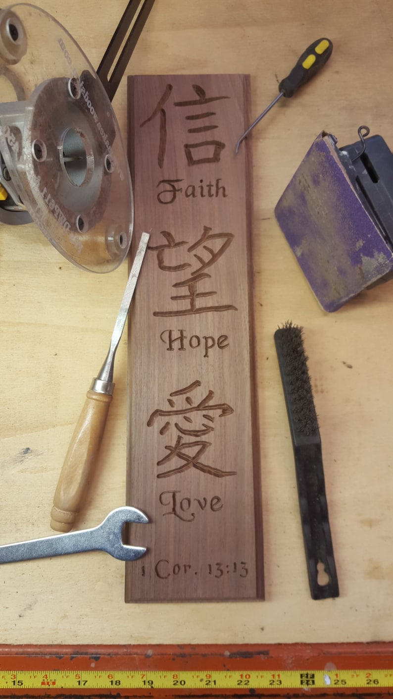 May include: A wooden sign with the words "Faith", "Hope", and "Love" carved into it. The words are in both English and Chinese characters. The sign also includes the Bible verse "1 Cor. 13:13".