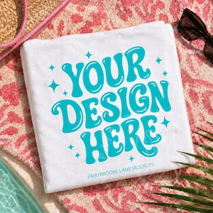 Peut inclure: Serviette de plage blanche avec le texte "YOUR DESIGN HERE" en turquoise, entouré d'étoiles. La serviette est posée sur une surface à motifs roses et rouges, avec des lunettes de soleil et un sac de paille en arrière-plan.