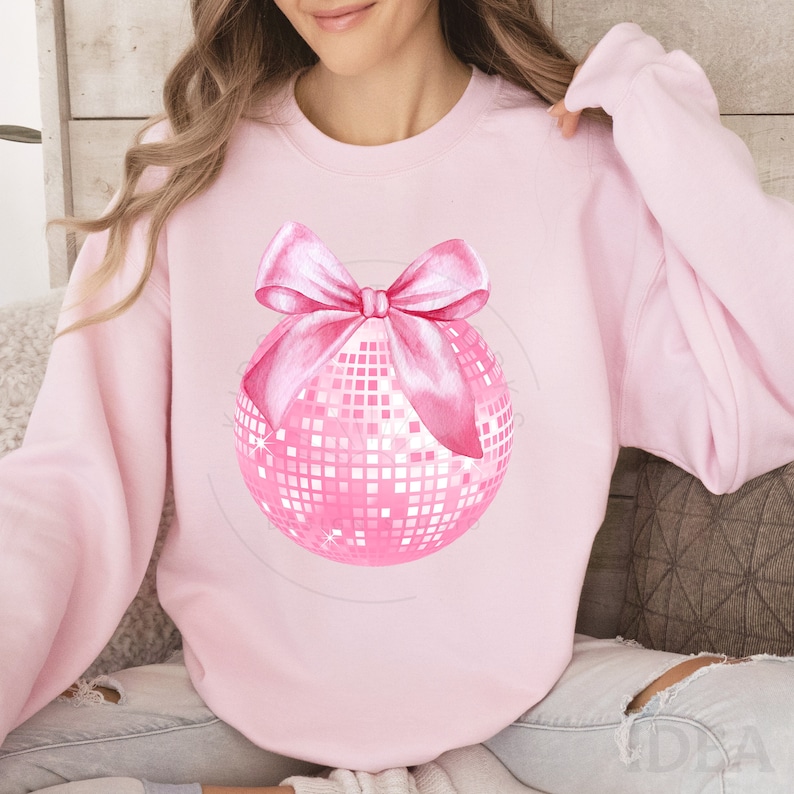 May include: Pink sweatshirt featuring a pink disco ball with a pink bow.