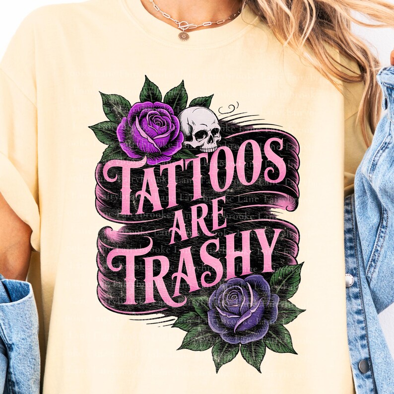 May include: Cream-colored t-shirt featuring a graphic design with the text "Tattoos Are Trashy" in pink script on a black banner. The design includes purple roses, green leaves, and a skull.