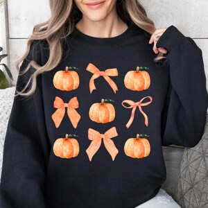 May include: Black sweatshirt with a pattern of orange pumpkins and orange bows.
