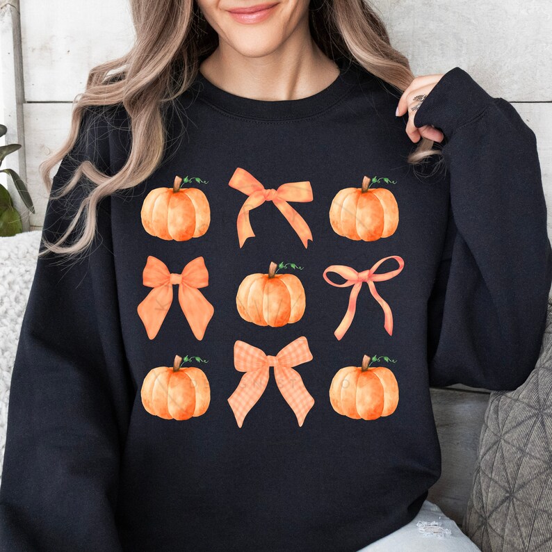 May include: Black sweatshirt with a pattern of orange pumpkins and orange bows.