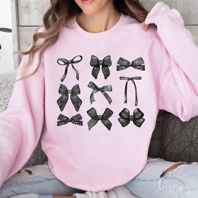 May include: A pink sweatshirt with a design of nine black bows in different styles. The bows are arranged in three rows of three.