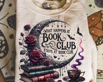 Könnte beinhalten: Ein beiges Sweatshirt mit einem Design mit einem Halbmond, Rosen, Büchern und einer Teetasse. Der Text lautet "What Happens at Book Club Stays at Book Club". Das Design umfasst Fledermäuse und eine lilafarbene Rauchwolke.