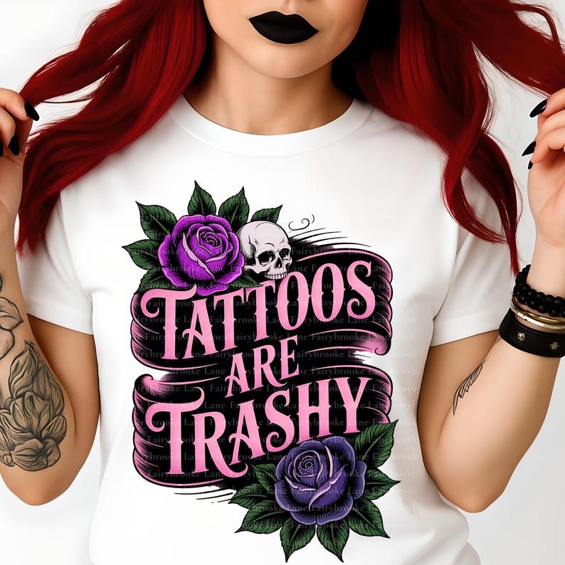 May include: White t-shirt featuring a graphic design with the text "Tattoos Are Trashy" in pink, accompanied by purple roses, green leaves, and a skull. The design is centered on the front of the shirt.