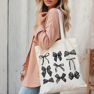May include: A white canvas tote bag with black and white illustrations of bows. The bag has a pink text overlay that says "Pretty Bows".