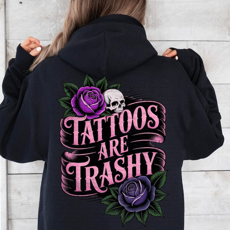 May include: Black hoodie with a graphic design on the back. The design features a skull, purple roses, and the text "Tattoos Are Trashy" in pink lettering. The hoodie is a dark color.